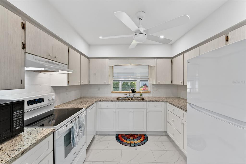 A kitchen features white cabinets, granite countertops, a white ceiling fan, and white appliances — 1735 LORALIN DRIVE, ENGLEWOOD, FL