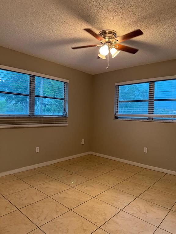 An empty room with beige walls, tile flooring, two windows, and a ceiling fan — 6080 22ND AVENUE N UNIT 5, ST PETERSBURG, FL