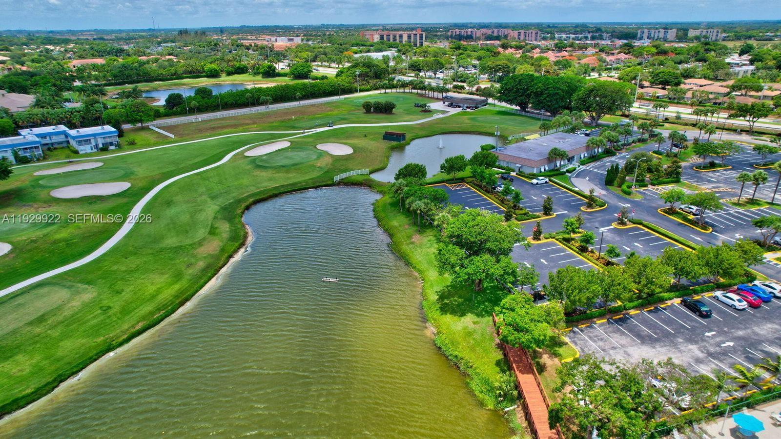 An aerial view shows a golf course with a large pond and an adjacent parking lot — 25 Saxony A # A, Delray Beach FL 33446, DELRAY BEACH, FL