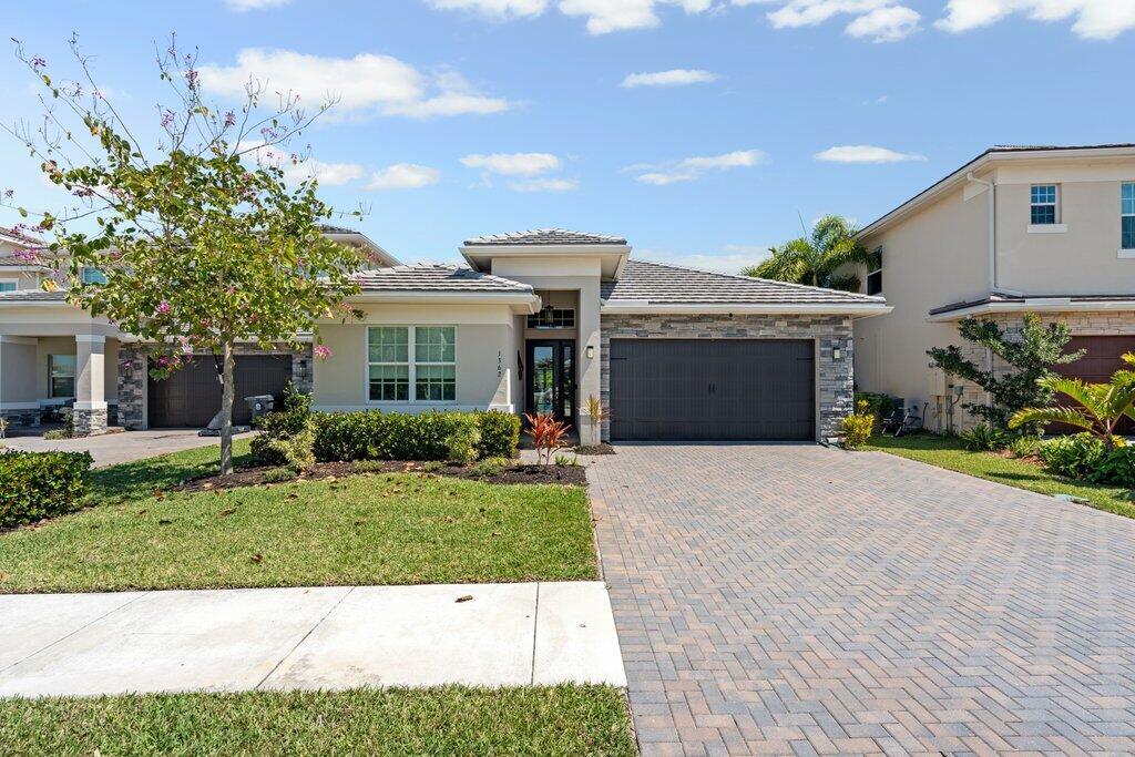 A single-story house with a stone facade, a dark garage door, and a paved driveway — 1362 Harvester Crossing, Loxahatchee FL 33470, LOXAHATCHEE, FL