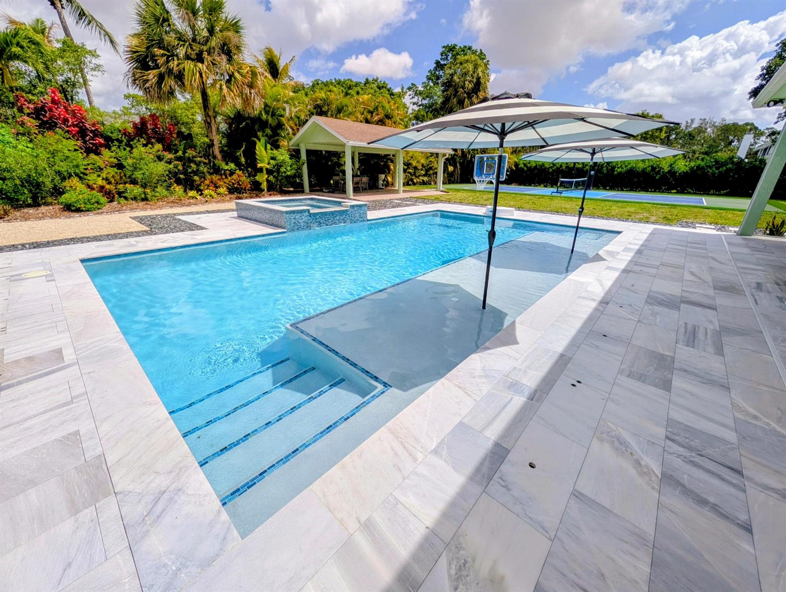 A rectangular swimming pool with a tanning ledge, hot tub, and two umbrellas on a patio — 8763 Pinion Drive, Lake Worth FL 33467, LAKE WORTH, FL