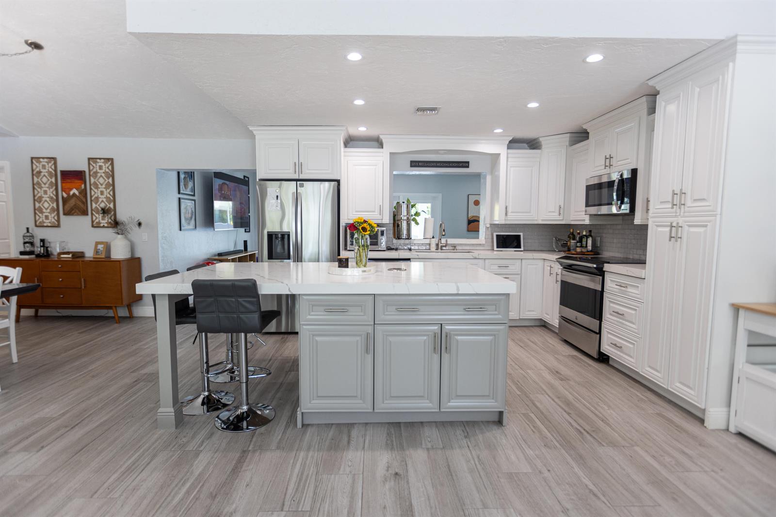 A kitchen features white cabinets, a gray island with a marble countertop, and wood-look flooring — 8763 Pinion Drive, Lake Worth FL 33467, LAKE WORTH, FL