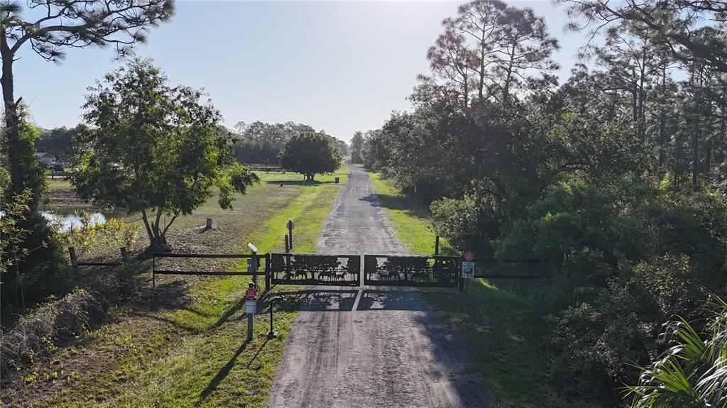 A gravel driveway leads to a decorative metal gate surrounded by trees and grassy fields — 14350 BURNT STORE ROAD, PUNTA GORDA, FL