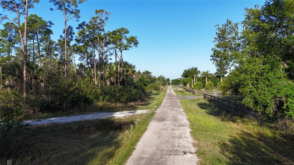 A gravel road stretches through a rural landscape with trees and a wooden fence — 14350 BURNT STORE ROAD, PUNTA GORDA, FL