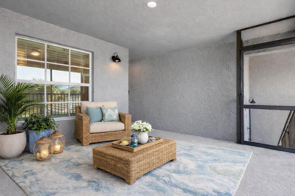 A covered patio features a wicker chair, coffee table, area rug, and a large window — 17475 OPAL SAND DRIVE UNIT 205, VENICE, FL