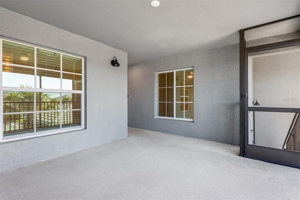 A covered outdoor patio features gray stucco walls, two windows, and a screened door — 17475 OPAL SAND DRIVE UNIT 205, VENICE, FL