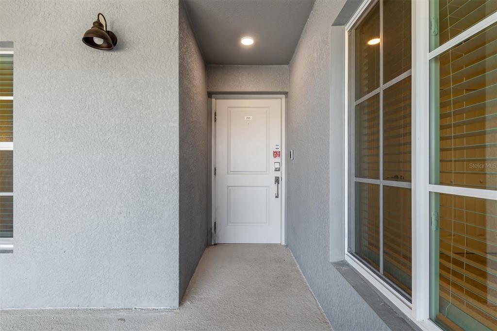 A white front door is centered in a gray stucco entryway with a wall-mounted light — 17475 OPAL SAND DRIVE UNIT 205, VENICE, FL