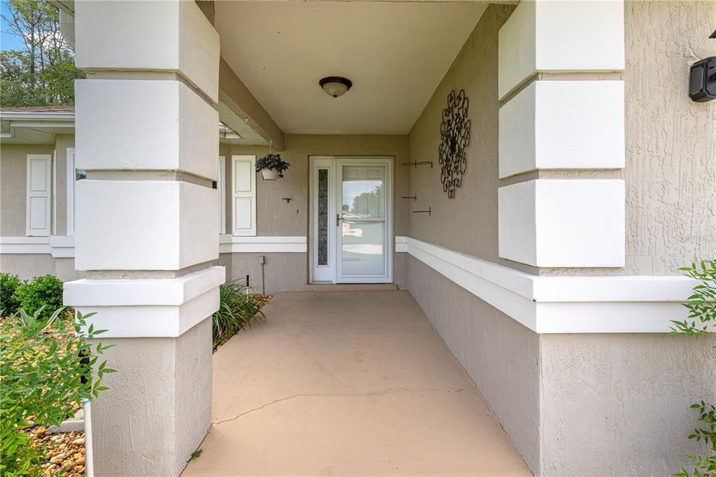 A covered entryway features a front door with a storm door and two large columns — 5968 SW 103 LOOP, OCALA, FL