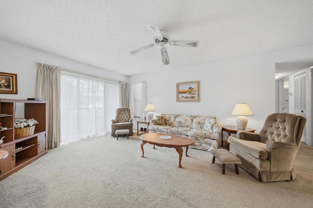 A living room features beige carpeting, a floral sofa, two armchairs, and a ceiling fan — 1441 PINE GLEN LANE UNIT E2, TARPON SPRINGS, FL