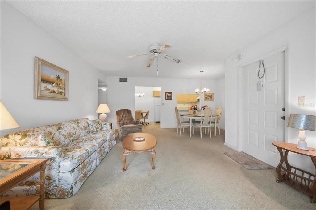 A living room with a floral sofa, a coffee table, and an adjacent dining area — 1441 PINE GLEN LANE UNIT E2, TARPON SPRINGS, FL