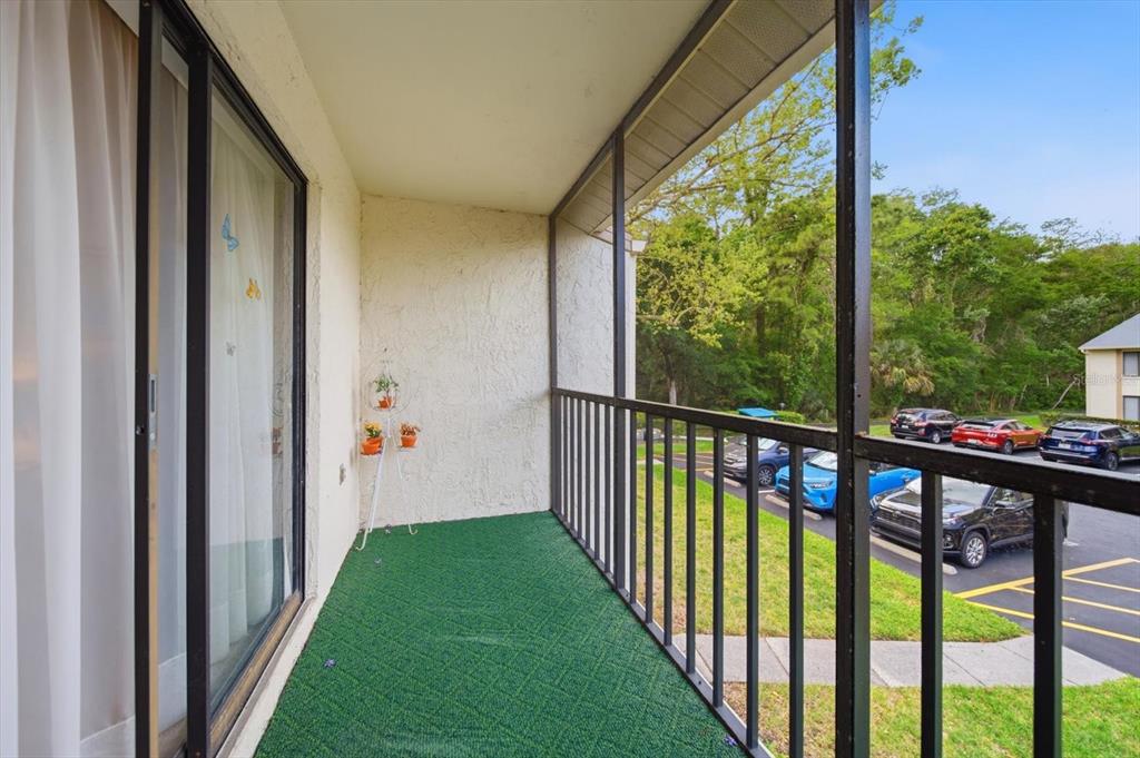 A screened-in balcony with green outdoor carpeting overlooks a parking lot and wooded area — 1441 PINE GLEN LANE UNIT E2, TARPON SPRINGS, FL