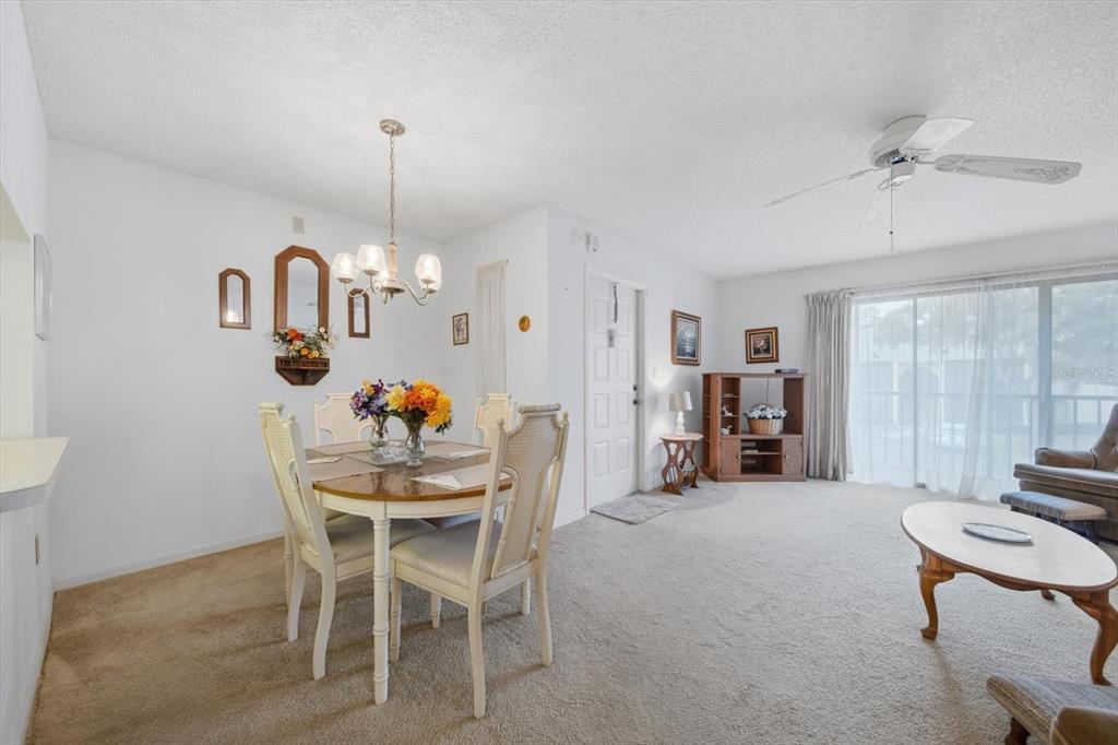 A dining area and living room with beige carpeting, white walls, and a ceiling fan — 1441 PINE GLEN LANE UNIT E2, TARPON SPRINGS, FL
