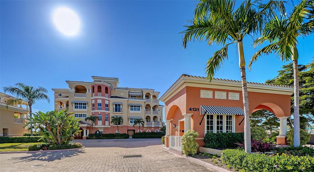 A multi-story apartment building stands behind a small gatehouse with a striped awning — 4127 GULF OF MEXICO DRIVE UNIT N102, LONGBOAT KEY, FL
