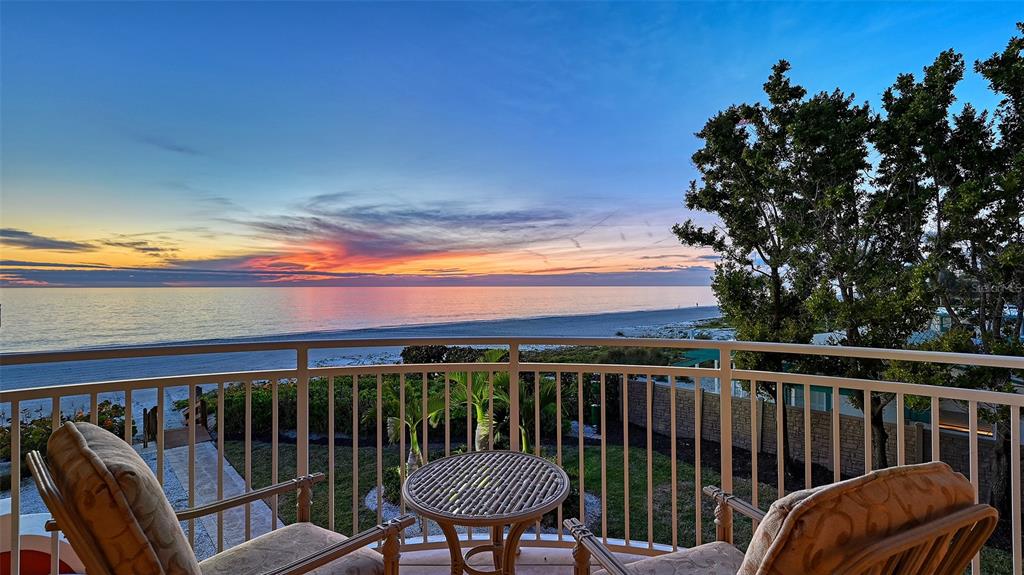 A balcony with two chairs and a small table overlooks a beach at sunset — 4127 GULF OF MEXICO DRIVE UNIT N102, LONGBOAT KEY, FL