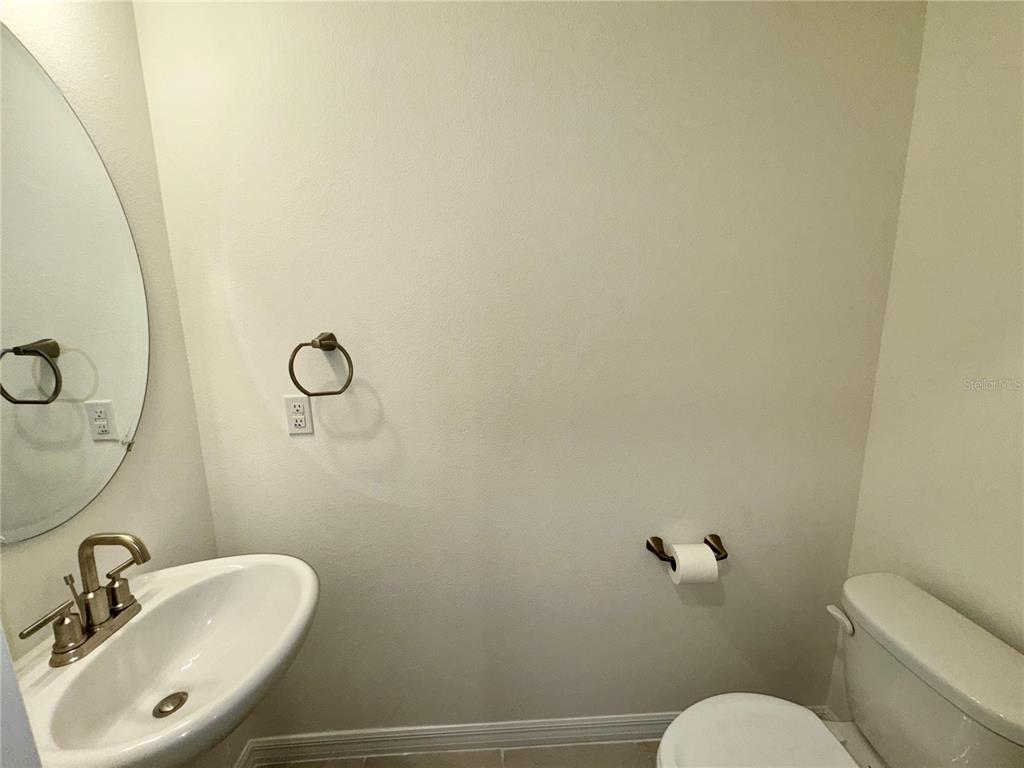 A small bathroom features a pedestal sink, a toilet, and a wall-mounted toilet paper holder — 4570 SMALL CREEK ROAD, KISSIMMEE, FL