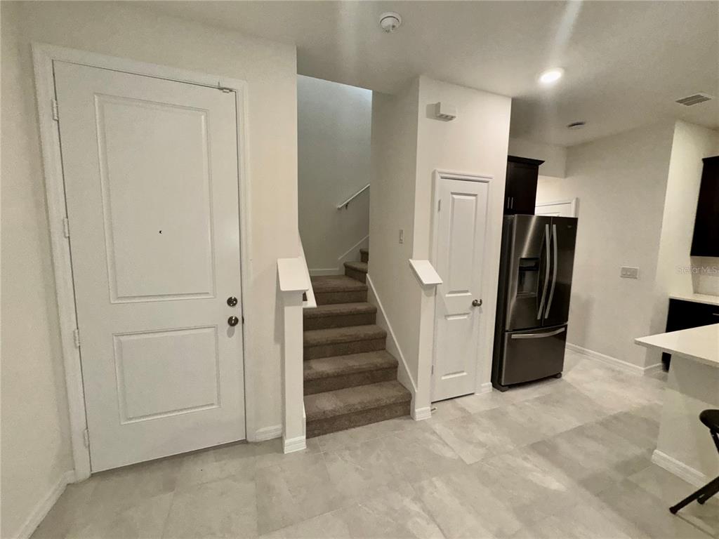 An interior view shows a tiled entryway with a staircase, a white door, and a refrigerator — 4570 SMALL CREEK ROAD, KISSIMMEE, FL