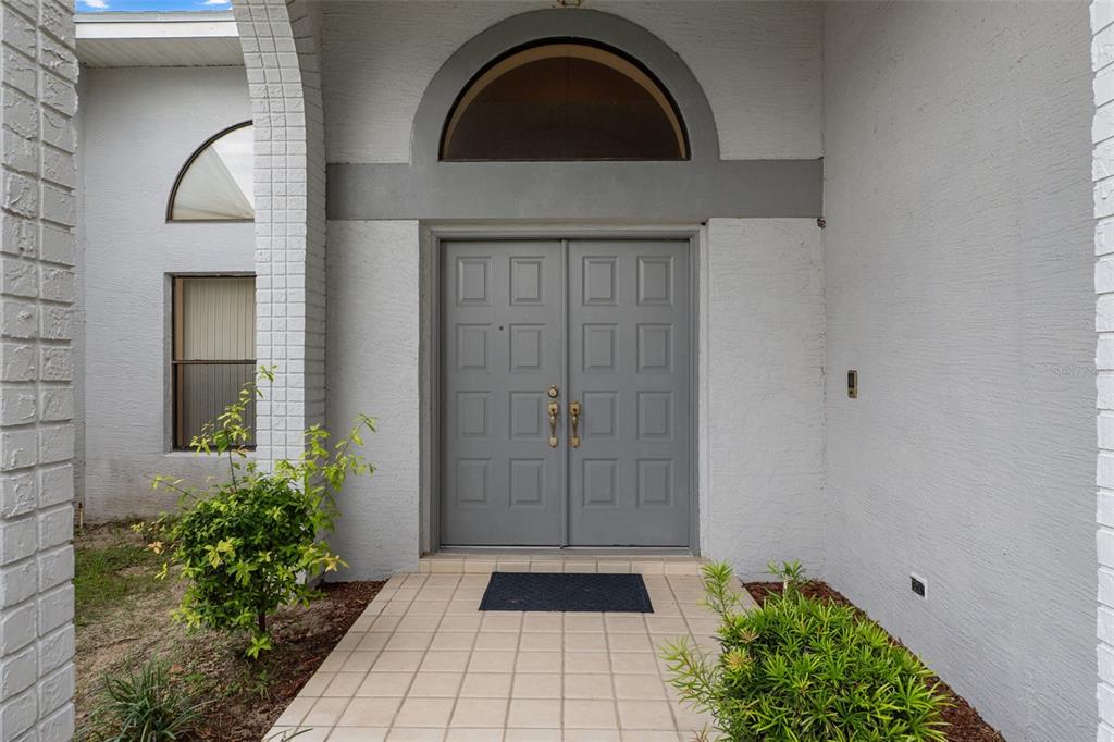 A gray double front door with a semi-circular transom window sits under a covered entryway — 3225 GLENWOOD CIRCLE, HOLIDAY, FL