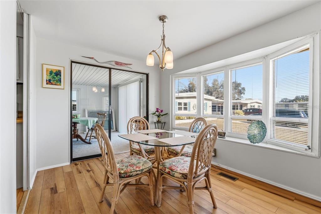 A dining area features a glass-topped rattan table, wood flooring, and a large bay window — 6581 HONU COURT, NORTH PORT, FL