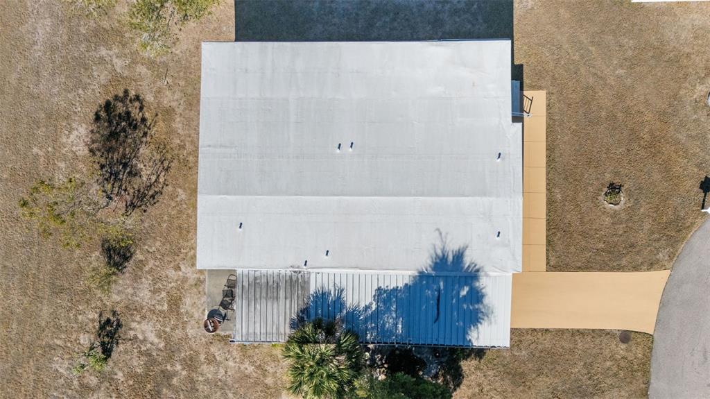 An aerial view shows a house with a white roof, a metal-covered porch, and a driveway — 6581 HONU COURT, NORTH PORT, FL