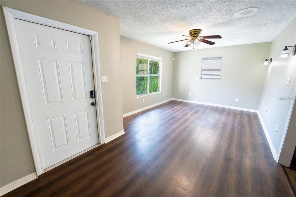 An empty room features dark wood-look flooring, light-colored walls, a ceiling fan, and a white door — 535 W DIVISION STREET, DELAND, FL
