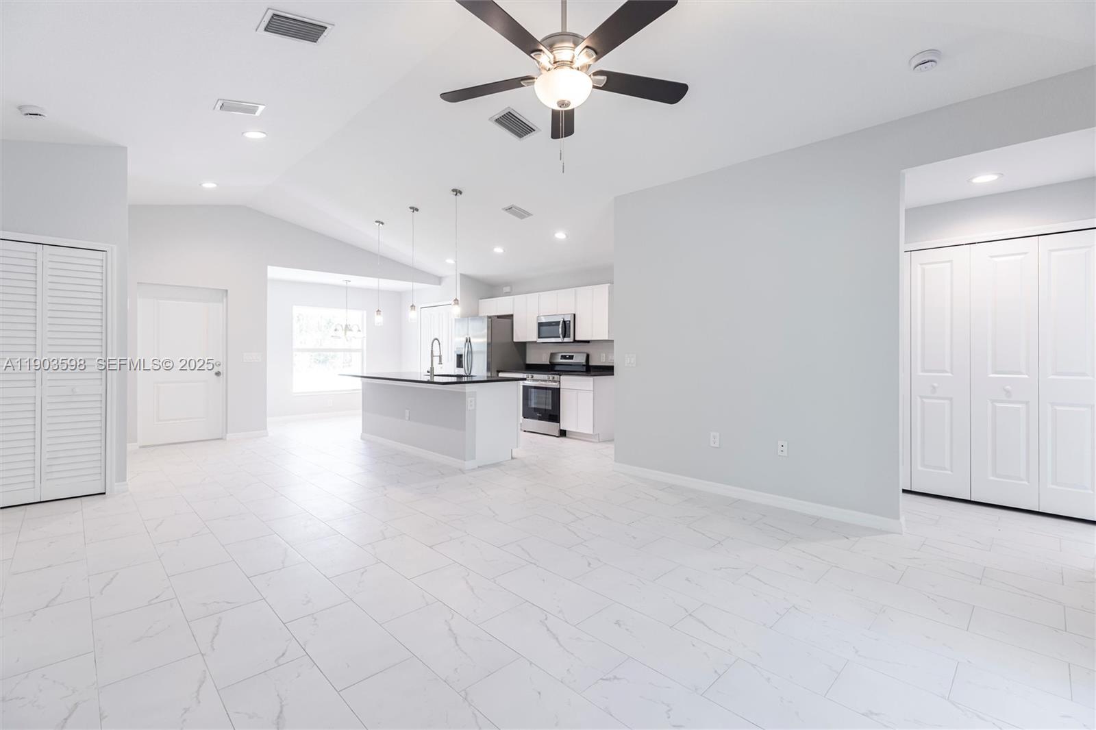 An open-concept kitchen and living area features white cabinetry, a kitchen island, and tiled floors — 2005 Rosa Ct, Lehigh Acres FL 33972, LEHIGH ACRES, FL