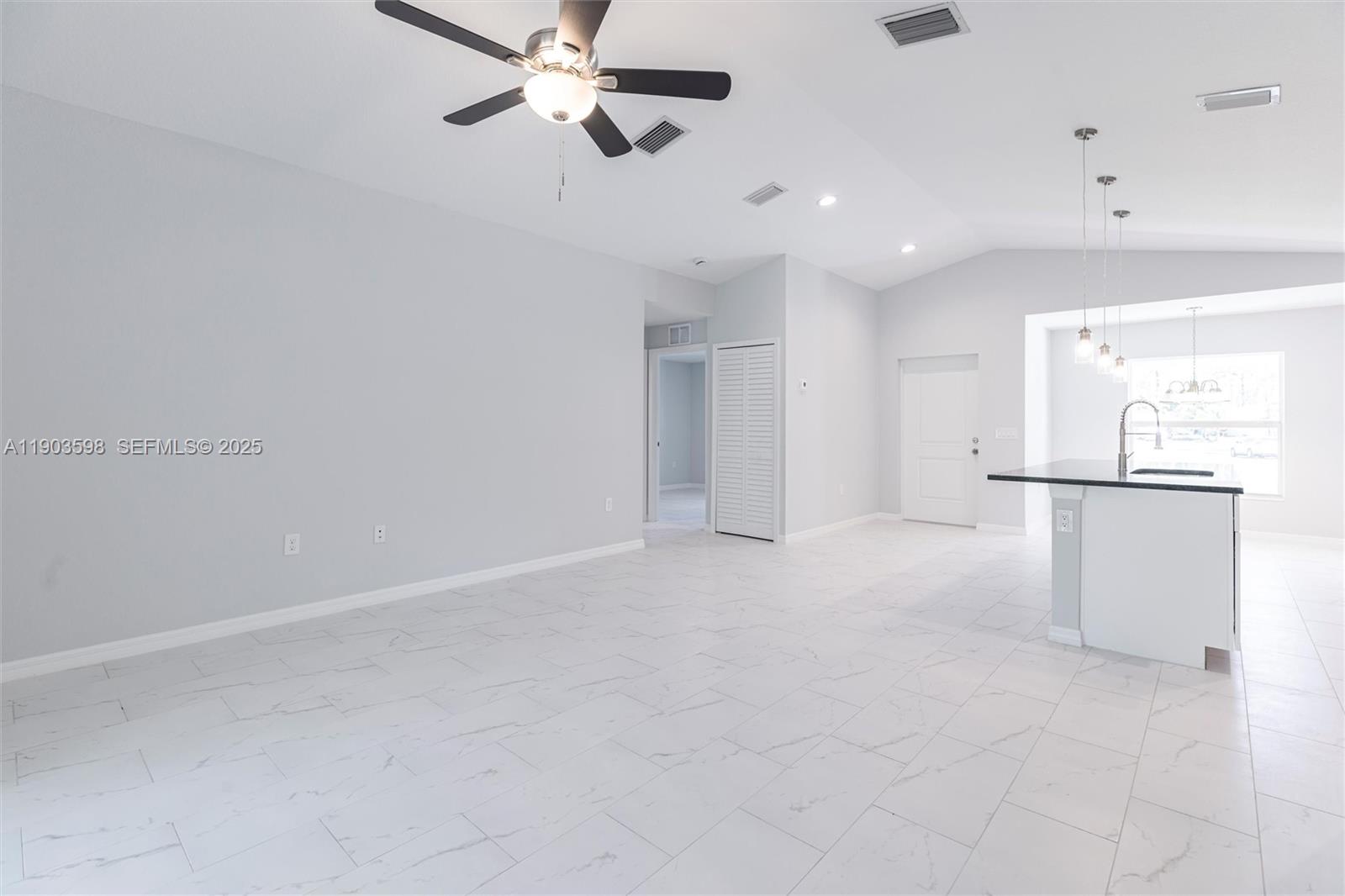 A bright, open-concept living area features white tile flooring, a ceiling fan, and a kitchen island — 2005 Rosa Ct, Lehigh Acres FL 33972, LEHIGH ACRES, FL