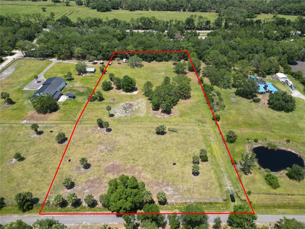 An aerial view shows a large, grassy, rectangular lot outlined in red with scattered trees — 1234 QUAIL RUN, OSTEEN, FL