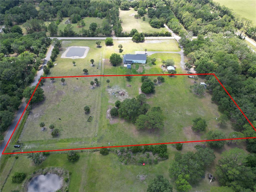 An aerial view shows a large, fenced grassy lot with scattered trees and a house — 1234 QUAIL RUN, OSTEEN, FL