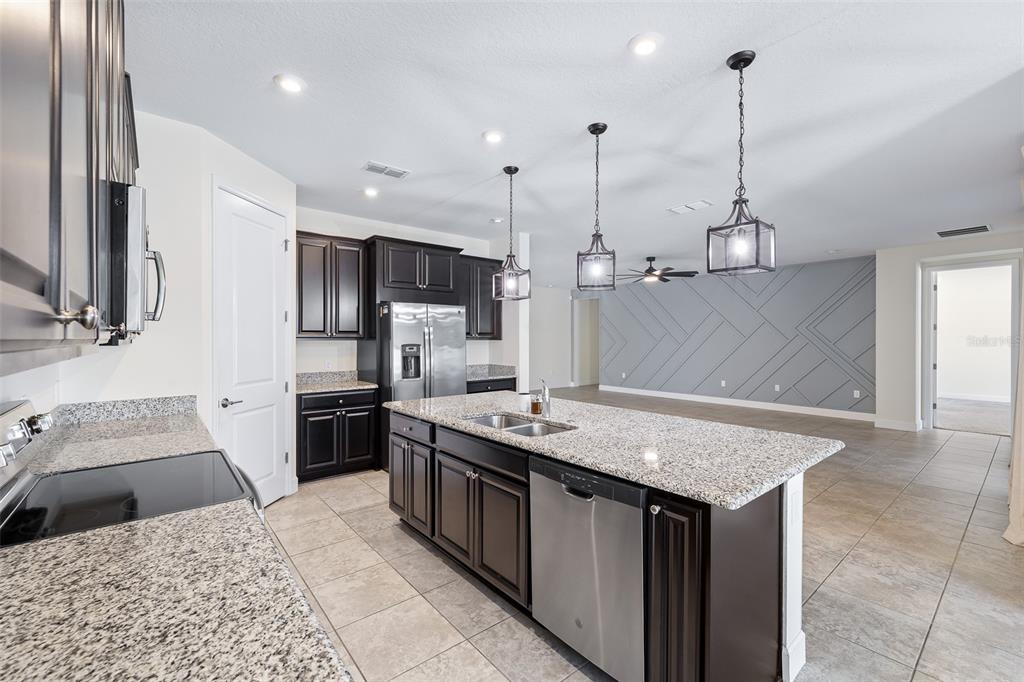 A kitchen island with granite countertops sits before a living area with a geometric wall — 3910 REDFIN PLACE, KISSIMMEE, FL