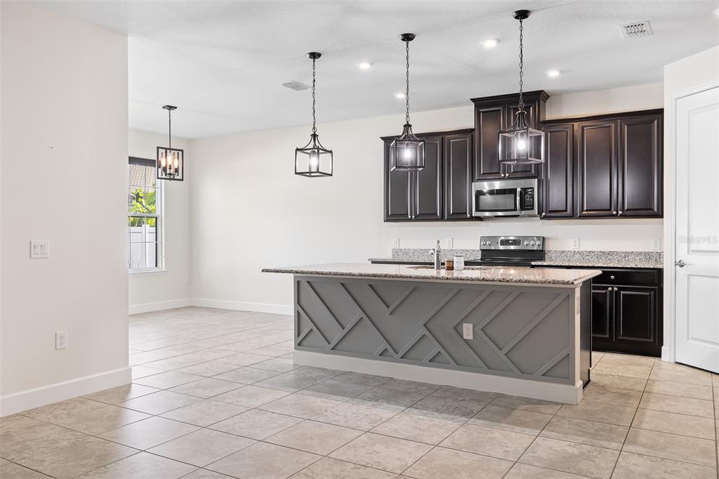 A spacious open-concept living area features light tile flooring, a kitchen island, and sliding doors — 3910 REDFIN PLACE, KISSIMMEE, FL