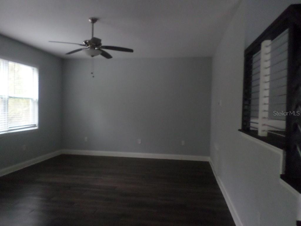 An empty room features gray walls, dark wood-look flooring, a ceiling fan, and two windows — 2773 RED WING VILLAGE, DELAND, FL