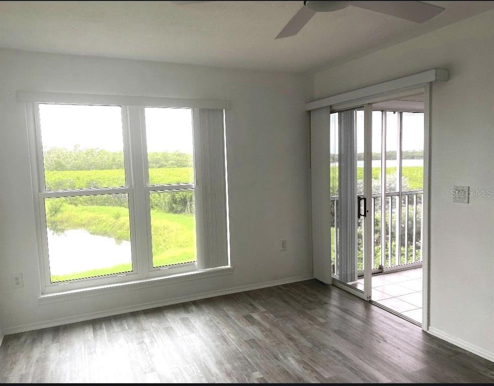 A room with wood-look flooring, large windows, and a sliding glass door leading to a balcony — 957 SANDPIPER CIRCLE UNIT 0, BRADENTON, FL