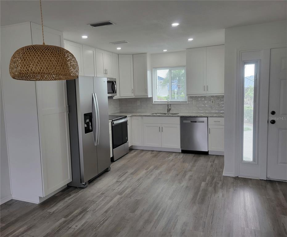 A kitchen features white cabinets, stainless steel appliances, granite countertops, and light wood-look flooring — 957 SANDPIPER CIRCLE UNIT 0, BRADENTON, FL