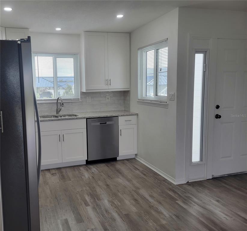 A kitchen with white cabinets, stainless steel appliances, granite countertops, and wood-look flooring — 957 SANDPIPER CIRCLE UNIT 0, BRADENTON, FL
