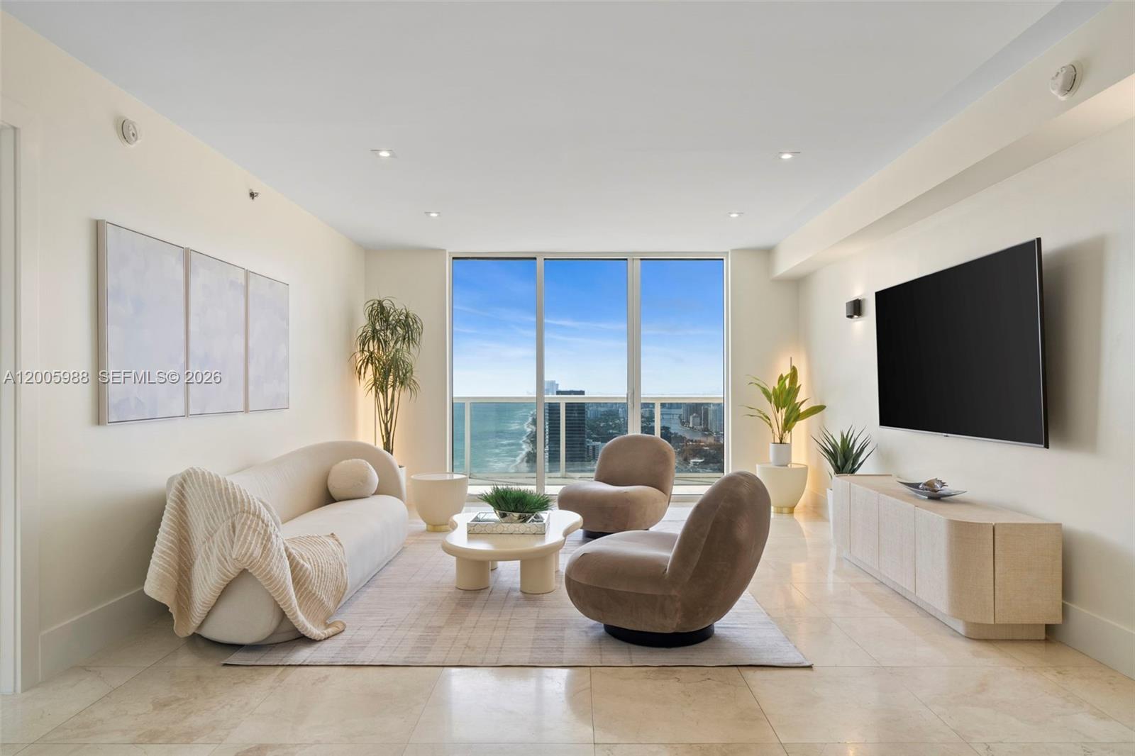 A modern living room features a curved sofa, two accent chairs, and a coastal view — 1830 S Ocean Dr # 5103, Hallandale Beach FL 33009, HALLANDALE BEACH, FL