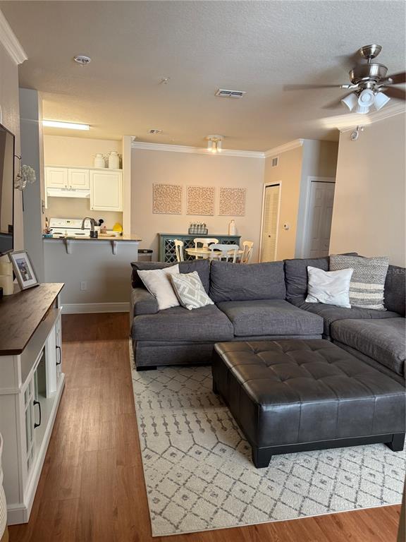 A living room with a gray sectional sofa, ottoman, and an adjacent open-concept kitchen — 1300 EASTERN PECAN PLACE UNIT 107, WINTER GARDEN, FL