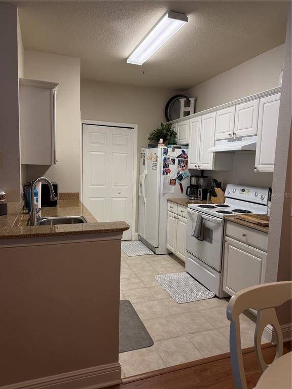 A kitchen features white cabinets, granite countertops, white appliances, and tile flooring — 1300 EASTERN PECAN PLACE UNIT 107, WINTER GARDEN, FL