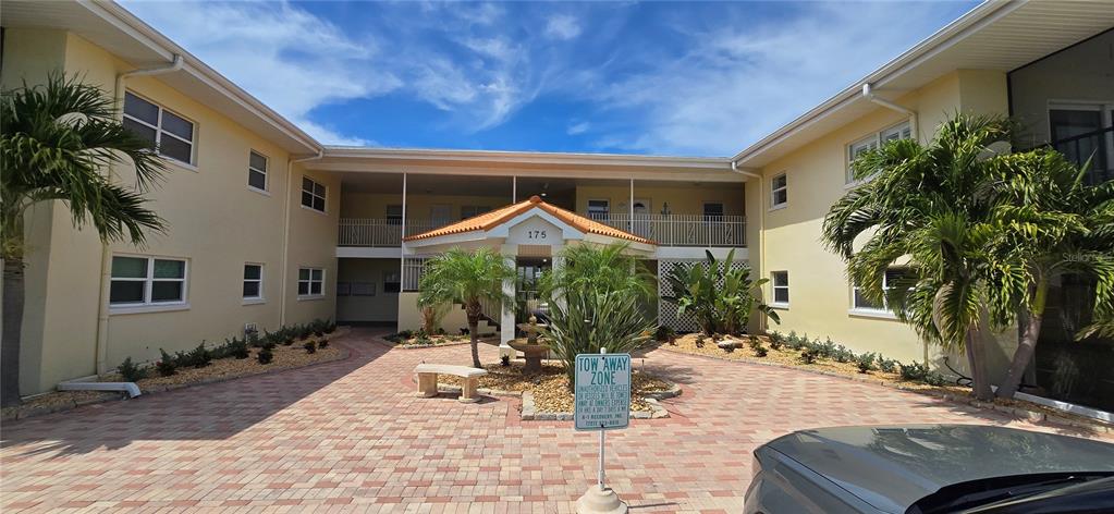 A paved courtyard leads to the entrance of a two-story apartment building with palm trees — 175 55TH AVENUE UNIT 204, ST PETE BEACH, FL