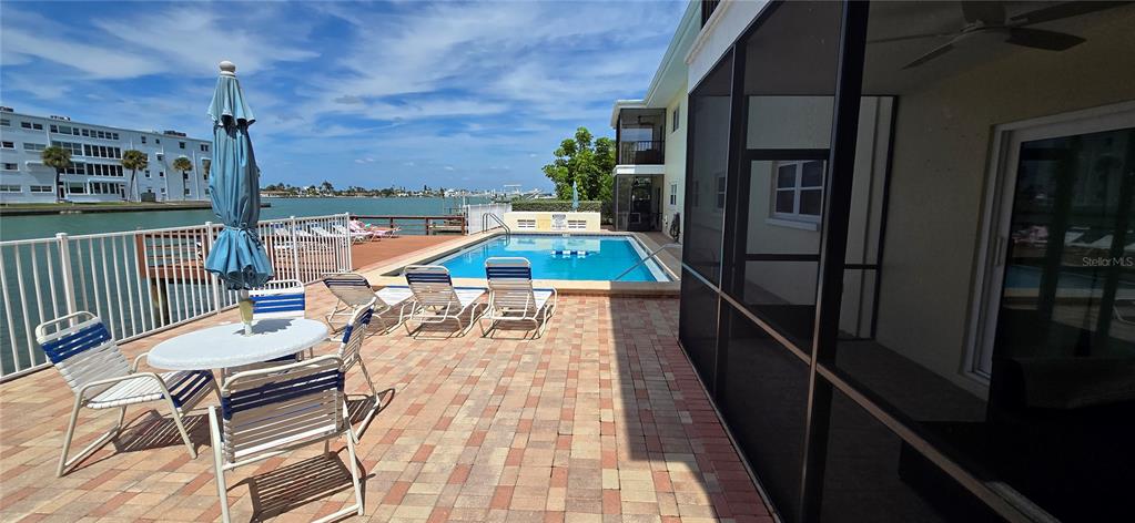 A patio with a pool, lounge chairs, and a table overlooks a waterfront area — 175 55TH AVENUE UNIT 204, ST PETE BEACH, FL