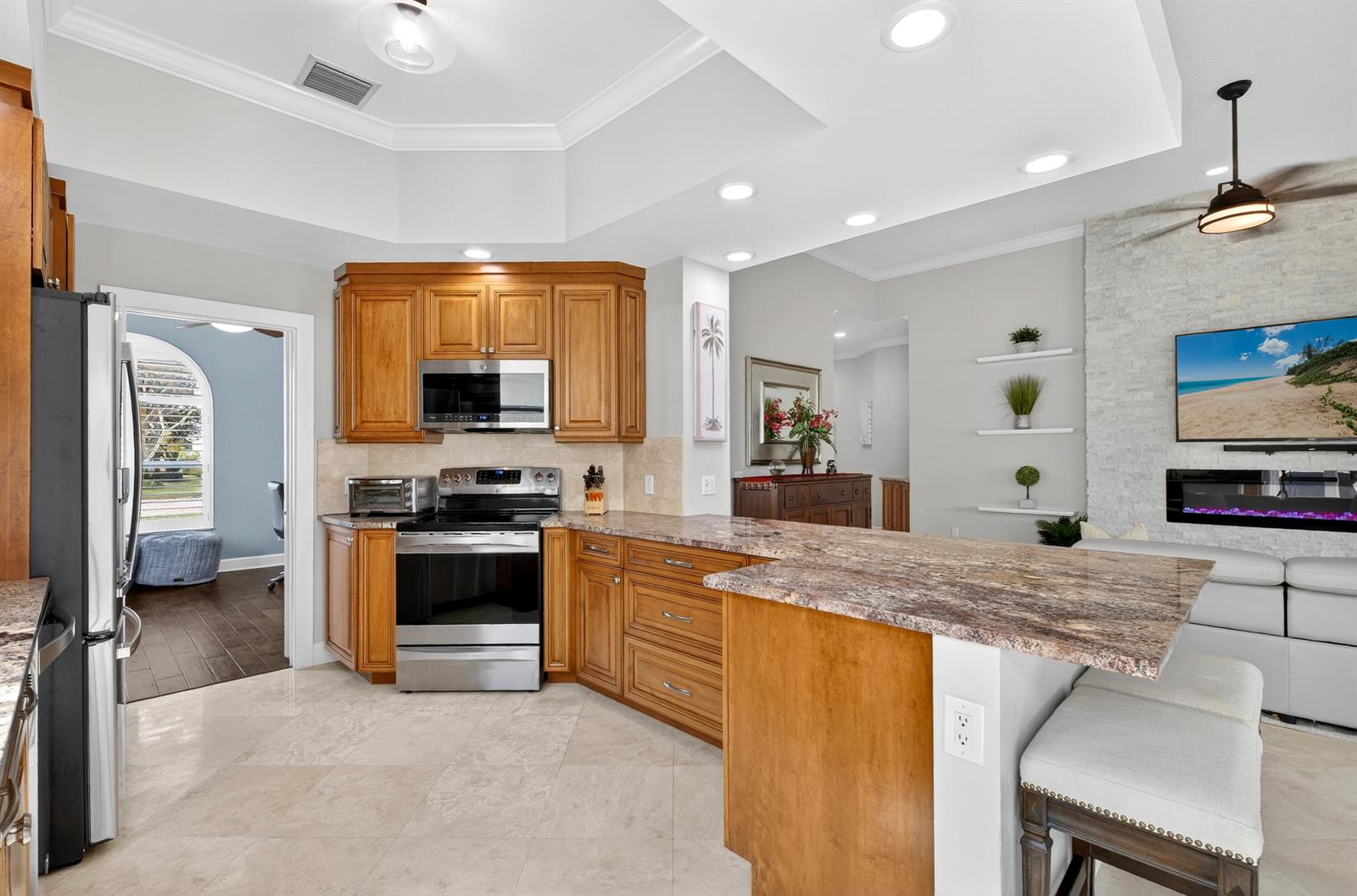 A kitchen with wood cabinets, granite countertops, and stainless steel appliances opens to a living area — 8223 Pine Cay Road, Wellington FL 33414, WELLINGTON, FL