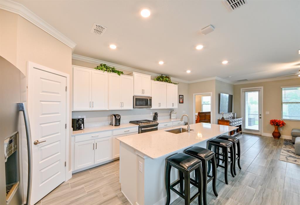 A modern kitchen features white cabinets, a quartz island with bar stools, and tiled floors — 8625 WINNING FIELDS ROAD, NEW PORT RICHEY, FL