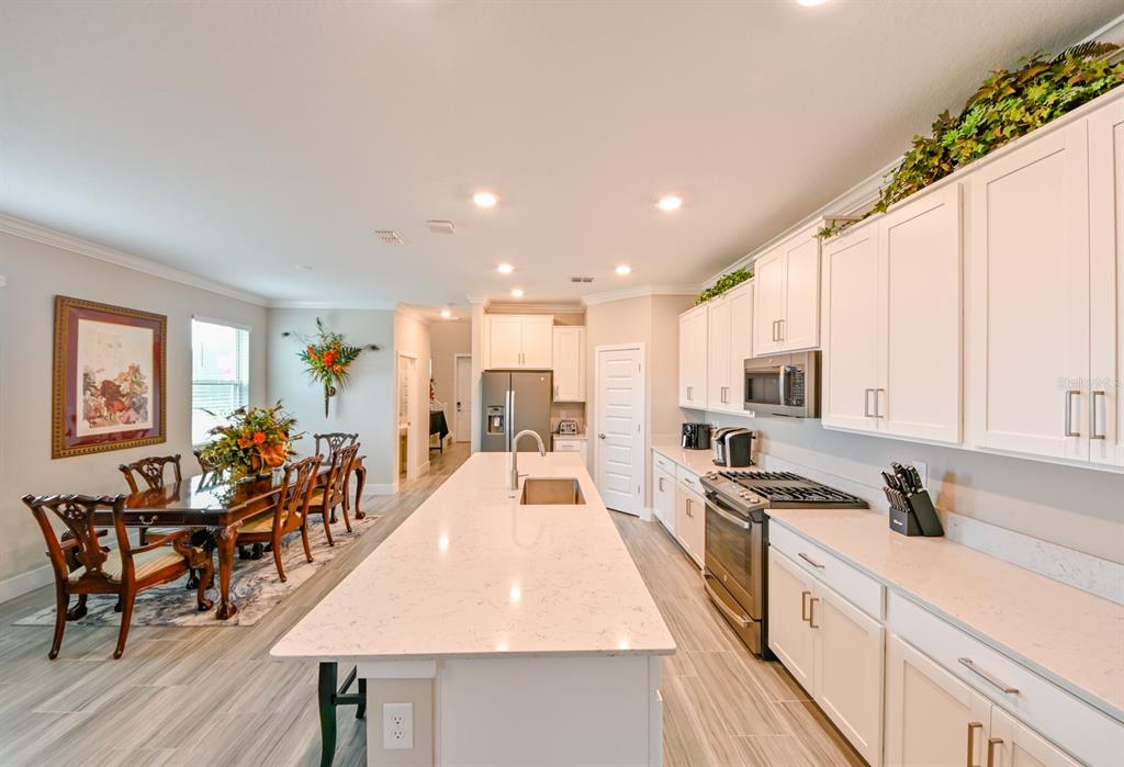 A kitchen with white cabinets, a large quartz island, and an adjacent dining area — 8625 WINNING FIELDS ROAD, NEW PORT RICHEY, FL