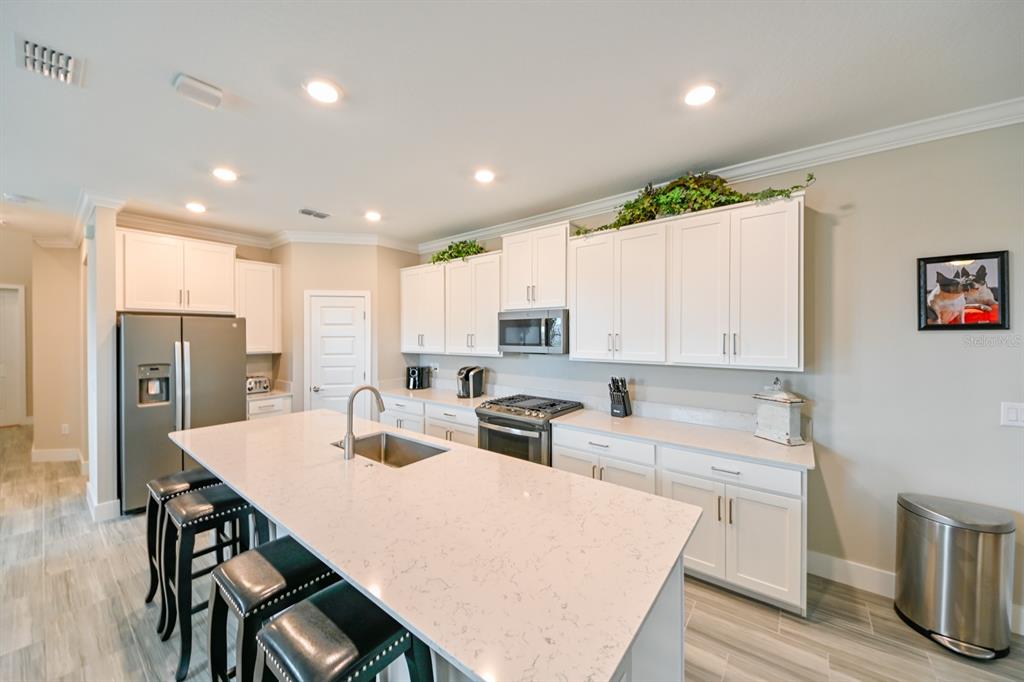A kitchen features white cabinets, a large quartz-topped island with seating, and stainless steel appliances — 8625 WINNING FIELDS ROAD, NEW PORT RICHEY, FL