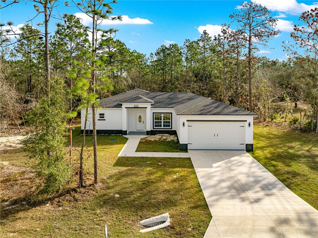 A white single-story house with a two-car garage sits on a lot surrounded by trees — 8311 SW 136TH TERRACE, DUNNELLON, FL