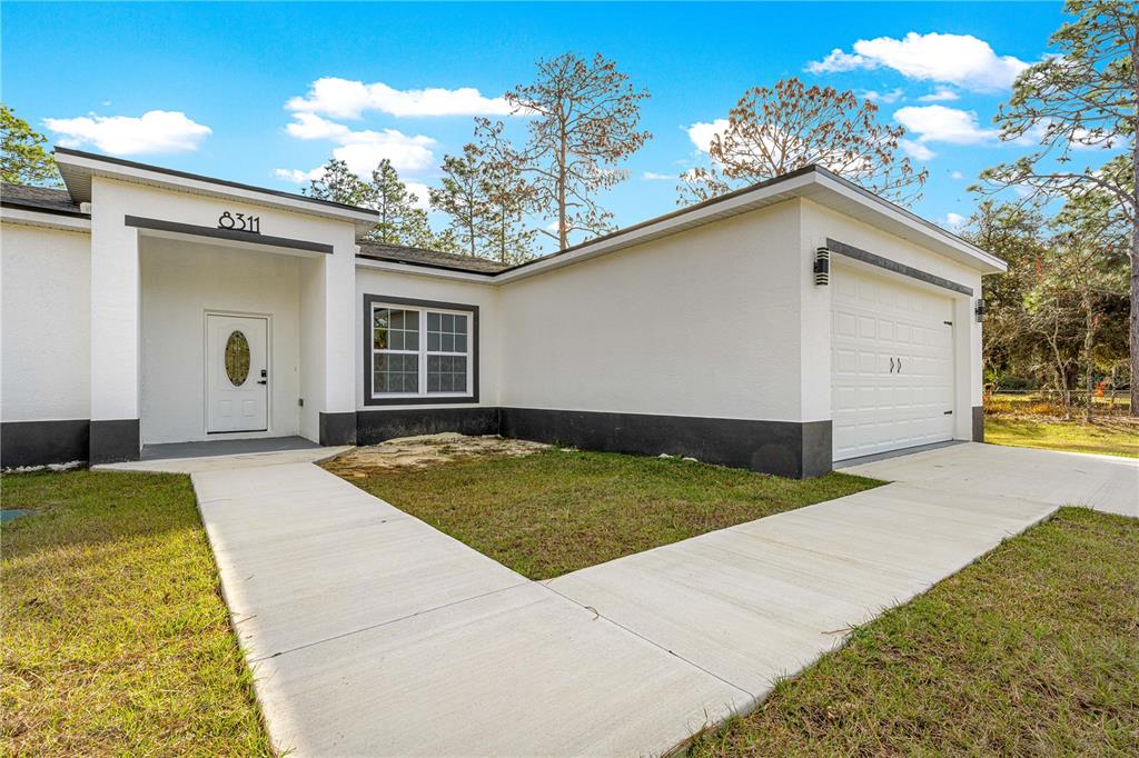 A single-story house with a white exterior, dark trim, a front porch, and a garage — 8311 SW 136TH TERRACE, DUNNELLON, FL
