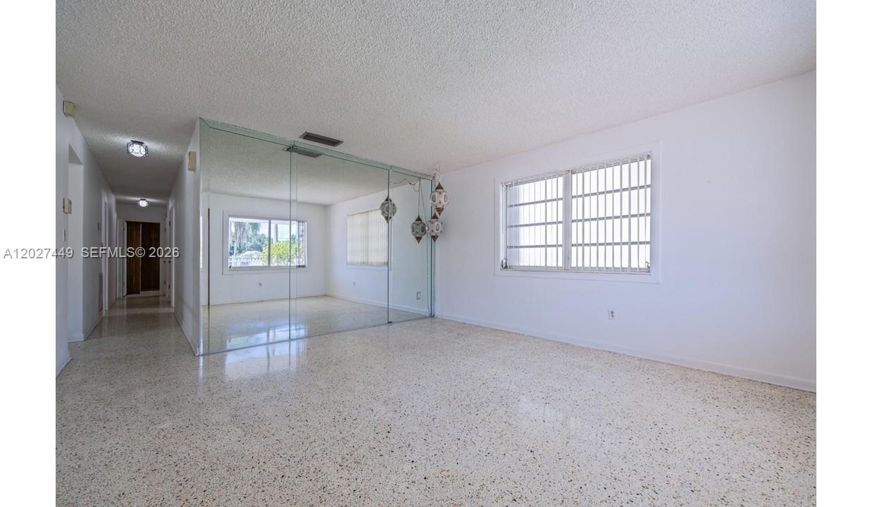 An empty room features terrazzo flooring, a mirrored wall, and windows with security bars — 3062 SW 14th St, Miami FL 33145, MIAMI, FL