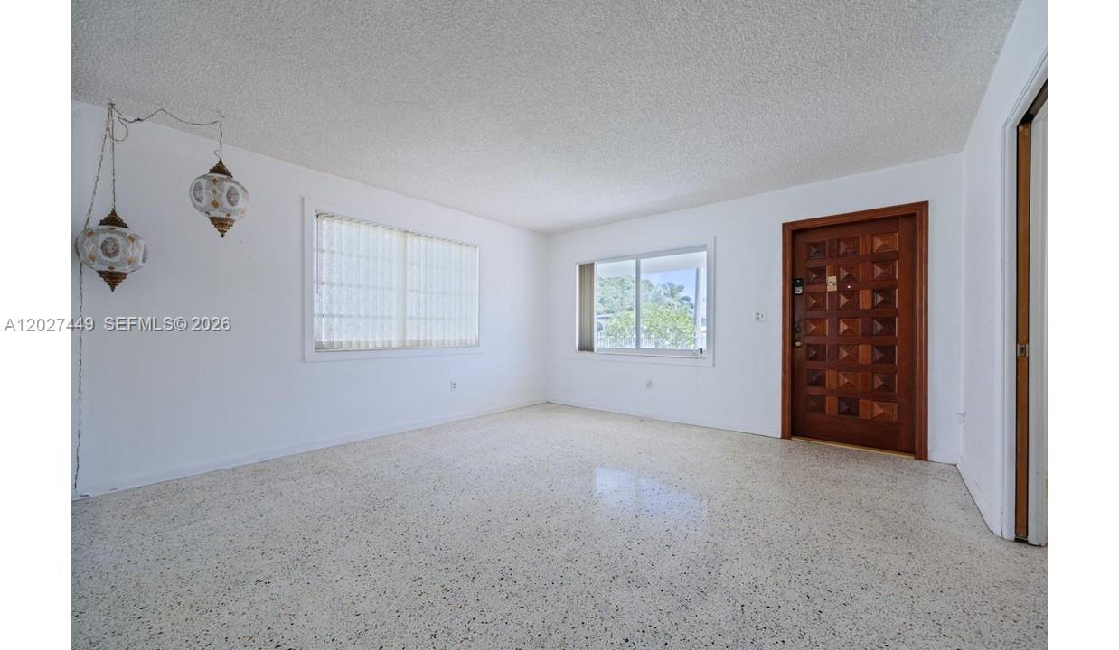 An empty room features white walls, a speckled terrazzo floor, and a wooden front door — 3062 SW 14th St, Miami FL 33145, MIAMI, FL