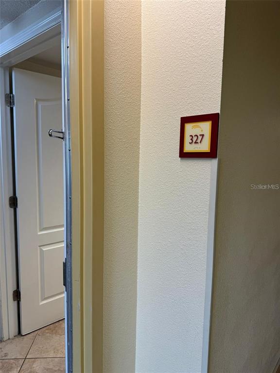A doorway leads into a room with a wall-mounted sign displaying the number 327 — 3000 MAINGATE LANE UNIT 327, KISSIMMEE, FL