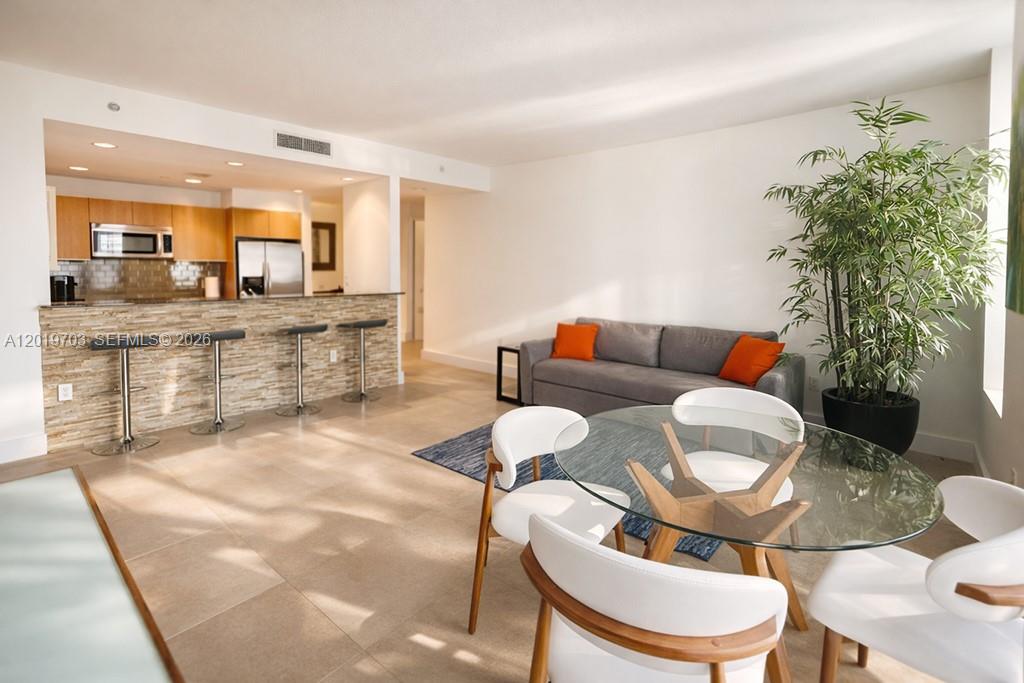 An open-concept living and dining area features a kitchen breakfast bar and tile flooring — 1050 Brickell Ave # 2210, Miami FL 33131, MIAMI, FL