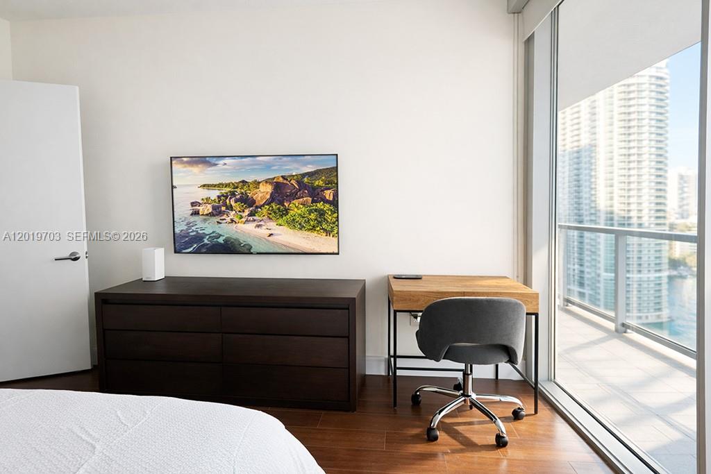 A bedroom features a dark wood dresser, a small desk, and a floor-to-ceiling window — 1050 Brickell Ave # 2210, Miami FL 33131, MIAMI, FL